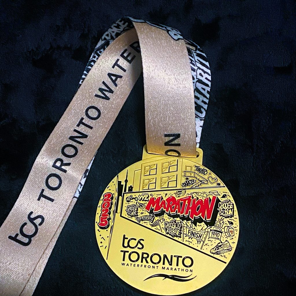 Close-up of the 2025 TCS Toronto Waterfront Marathon finisher’s medal with stylized comic-book design and gold finish.