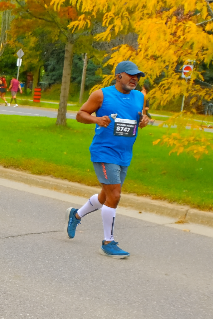 Runner in blue singlet and white compression socks maintaining pace during the TCS Toronto Waterfront Marathon, with autumn leaves in the background.